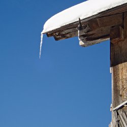 Eiszapfen am Hausdach, blauer Himmel